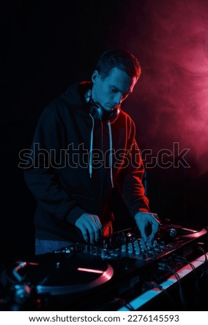Cool young DJ playing vinyls on party. Disk jokey mixing musical tracks in dark night club Royalty-Free Stock Photo #2276145593