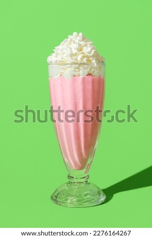 Close-up with a glass of strawberries milkshake topped with whipped cream. Delicious milkshake in bright light minimalist on a vibrant green table. Royalty-Free Stock Photo #2276164267