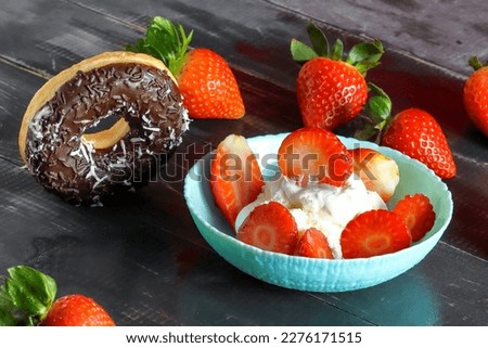 Ice cream in a plate stands on a wooden dark table. Strawberries, donut