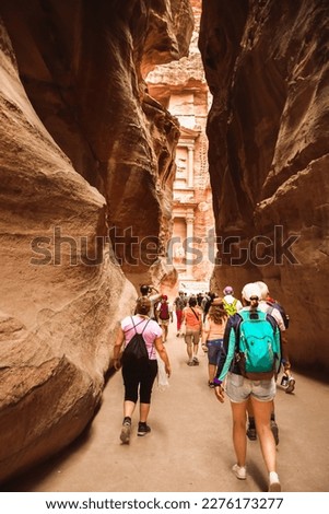 Tourists walk towards treasury landmark in Petra through The Siq, the narrow slot-canyon that serves as the entrance passage to the hidden city of Petra, Jordan Royalty-Free Stock Photo #2276173277