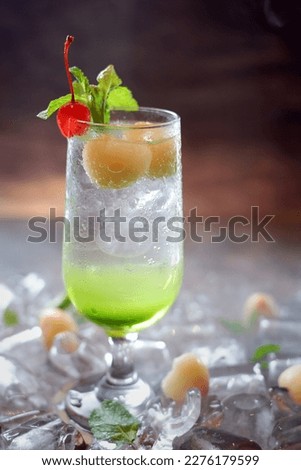 A green cocktail with ice and a cherry on the top