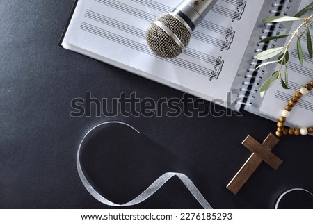 Choral music background for Palm Sunday with sheet music, microphone and olive branches with a Christian cross on a black table. Top view.