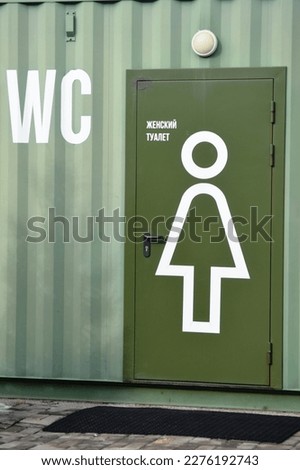 toilet sign in front of a green wall with a toilet door. The inscription on the door in Russian "Women's toilet"