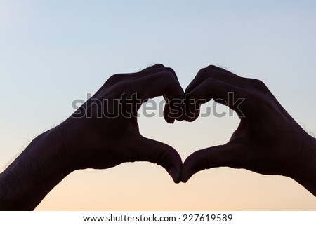 Love sign. Heart symbol by hand silhouette in sunset sky. Vintage style background