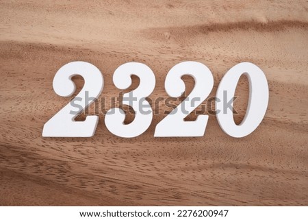 White number 2320 on a brown and light brown wooden background.

