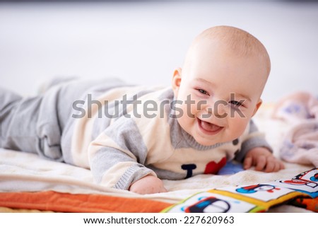 Happy gurgling baby lying on his bed playing with colorful pictures in a book looking at the camera with an adorable beaming smile of contentment