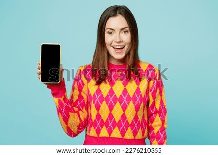 Young smling happy cheerful woman wears bright casual clothes hold in hand use mobile cell phone with blank screen workspace area isolated on plain pastel light blue cyan background studio portrait