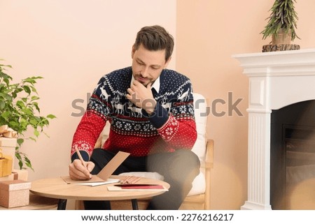 Man writing wishes in Christmas greeting card in living room