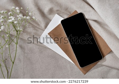 Mobile phone, smartphone, paper cards and flowers on a neutral beige linen background, elegant aesthetic minimalist workspace, brand template with copy space