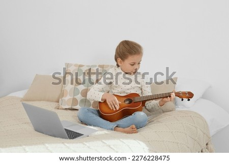 Little girl learning to play ukulele with online music course at home. Space for text
