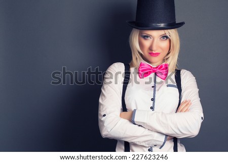 beautiful young woman wearing tophat, bow-tie and braces against grey background
