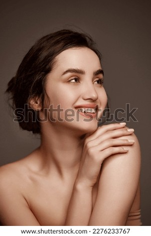 Attractive smile, tenderness. Portrait of young beautiful girl with brown hair posing over dark grey studio background. Concept of natural beauty, skincare, cosmetology, plastic surgery, health
