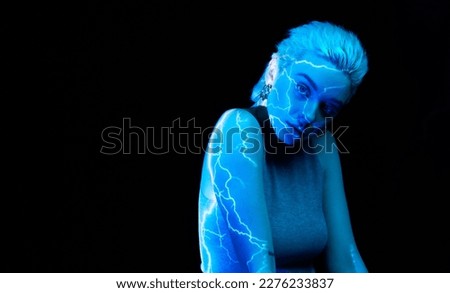 Lightening. Portrait of young blonde girl with abstract neon stripes on body posing over dark background in blue neon lights. Concept of art, modern style, cyberpunk, futurism and creativity