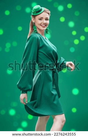 Cute young woman in a green hat and a green dress for a Saint Patrick's Day. Studio portrait on a green background with sparkles. 
