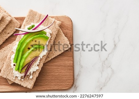Crispbread with cream cheese and avocado on a wooden cutting board. Top view. Copy space. Royalty-Free Stock Photo #2276247597