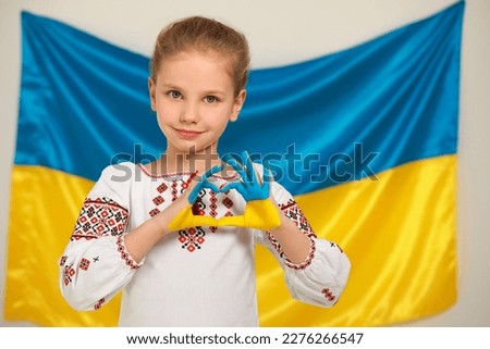 Little girl making heart with her painted hands near Ukrainian flag, space for text. Love Ukraine concept