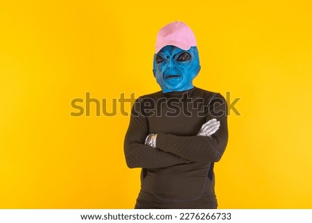 Man with blue headed alien mask, wearing a pink cap, arms crossed. Concept of bizarre, extraterrestrial, funny, strange and weird.