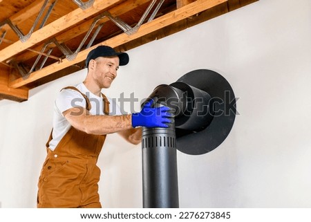 A male worker preparing a chimney installation for a modern, energy saving heating stove. Royalty-Free Stock Photo #2276273845