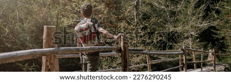 Rear on man traveler with backpack standing on bridge over river in forest. Traveling concept.