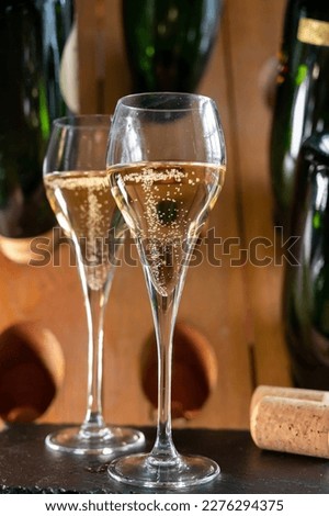 Glasses of sparkling white wine champagne gran cru or cava with bubbles and classic wooden champagne pupitre rack with empty bottles on background Royalty-Free Stock Photo #2276294375