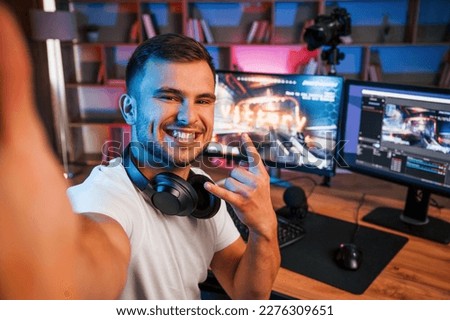 Making selfie, celebrating victory. Male game streamer in casual clothes is indoors with pc. Royalty-Free Stock Photo #2276309651