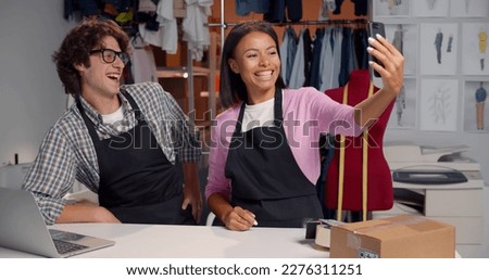 Happy fashion store warehouse workers having fun and taking selfie on smartphone. African and caucasian managers taking photo together on cellphone working in tailor storehouse