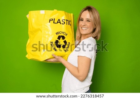 recycling, waste sorting and sustainability concept - smiling young woman in white t-shirt holding rubbish bin with plastic bottles and trash bag over green background