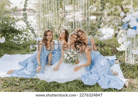 The bridesmaids are in blue dresses, the bride is holding a beautiful bouquet. Sitting enjoying the celebration. Beautiful luxury wedding blog concept. Spring wedding. Royalty-Free Stock Photo #2276324847