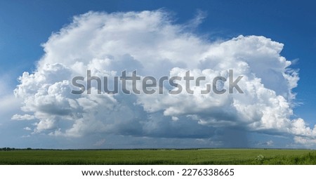 Big white cloud over a summer field that casts a shadow.
A large green field before the rain.
