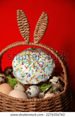Easter celebration. Easter decorations in a basket with rabbit ears. Easter cake and eggs on moss, quail eggs and feathers on a red background. Traditions and religion