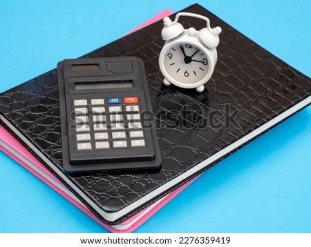 A stack of books with an old school calculator and an alarm clock as a concept for summing up, planning for retirement and doing business