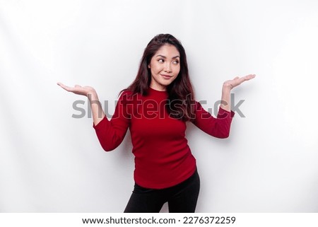 Excited Asian woman dressed in red, pointing at the copy space beside her, isolated by white background Royalty-Free Stock Photo #2276372259