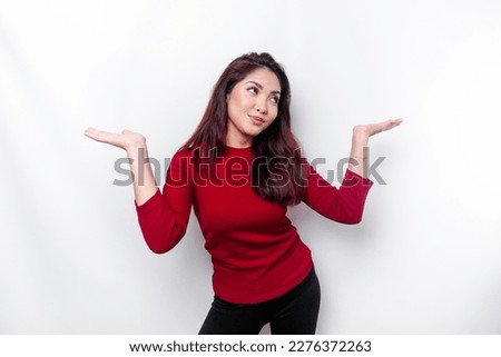 Excited Asian woman dressed in red, pointing at the copy space beside her, isolated by white background Royalty-Free Stock Photo #2276372263