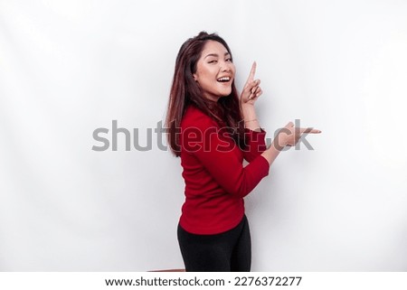 Excited Asian woman dressed in red, pointing at the copy space beside her, isolated by white background Royalty-Free Stock Photo #2276372277