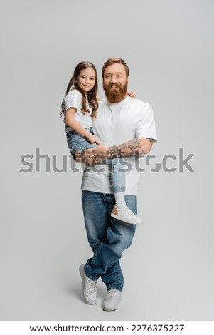 Full length of positive father in t-shirt and jeans holding daughter on grey background Royalty-Free Stock Photo #2276375227