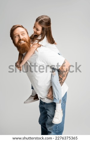 Cheerful kid piggybacking on tattooed father with beard isolated on grey Royalty-Free Stock Photo #2276375365