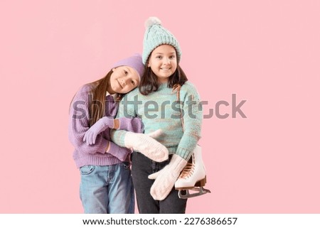 Little girls in winter clothes with ice skates hugging on pink background