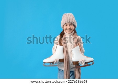 Little girl in winter clothes with ice skates on blue background