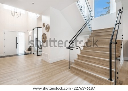 front door foyer entrance to an interior of a home with hardwood flooring beamed ceiling glass wall stair case view to home office and black metal stair railing Royalty-Free Stock Photo #2276396187