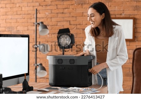 Young woman with portable power station at table in office