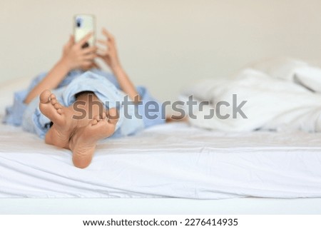 Woman lying on her bed with her legs facing the camera, absorbed in smartphone screen. Addictive nature of social media has captured her attention, pulling her away from reality and to digital world.