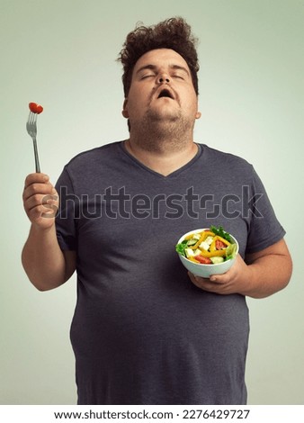 I wish this would turn into a burger. Studio shot of an overweight man holding a bowl of salad. Royalty-Free Stock Photo #2276429727