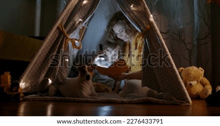 Happy caucasian mom and her cute baby boy spending time together at home, reading a book, using a flashlight in a cozy tent - happy family  Royalty-Free Stock Photo #2276433791