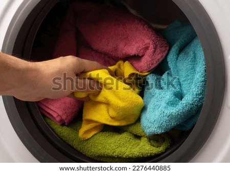 Hand and puts the laundry into the washing machine. focus on a colored towel. the hand takes things out of the washing machine after washing. Bright colorful things in the wash Royalty-Free Stock Photo #2276440885
