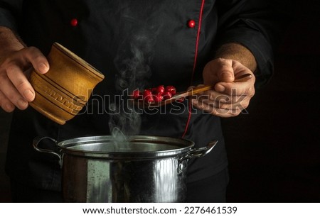 The cook adds dry rose hips to boiling water in a pot to make a medicinal tea. Folk medicine idea with space on black background Royalty-Free Stock Photo #2276461539