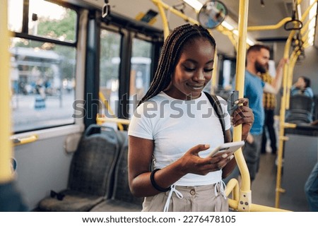 Portrait of a beautiful young African american woman using a smartphone while standing alone on a bus. Traveling to work and enjoying a bus ride. Black female using public transportation. Copy space. Royalty-Free Stock Photo #2276478105