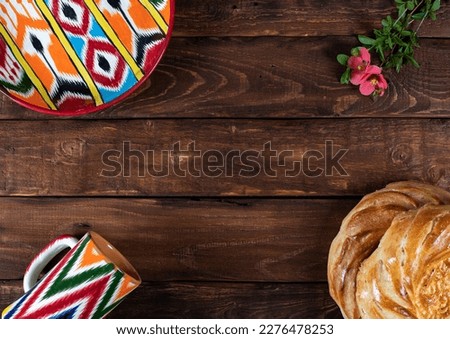 Rishtan Uzbek national plate and mug, journey cake bread and pink flowers on wooden background. Postcard for Navruz, Kurban bayram