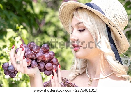 Photo of a young blonde woman in a hat, who is holding a bunch of grapes in her hand. Outdoor recreation,summer picnic.