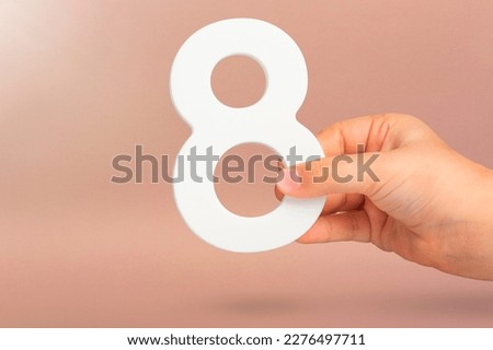 Eight in hand. A hand holds a white number 8 on a red background. Concept with number eight. Birthday 8 years, percentage, eighth grade or day, international women's day. Royalty-Free Stock Photo #2276497711