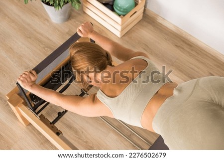 Woman training pilates on the reformer bed. Reformer pilates studio machine for fitness workouts in gym. Fit, healthy and strong authentical body. Fitness concept